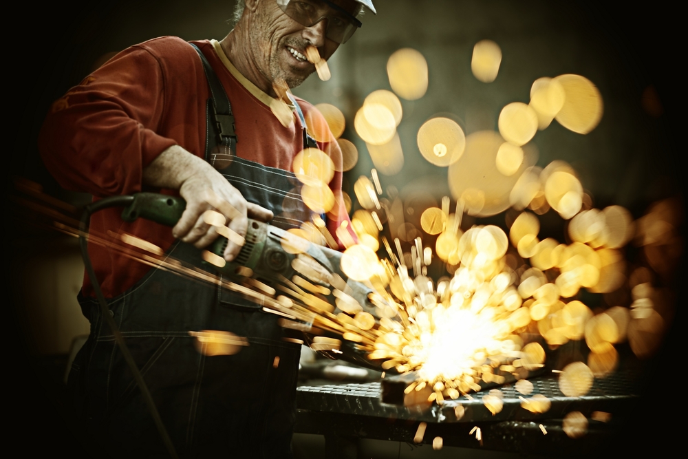 Industrial worker cutting and welding metal with many sharp sparks