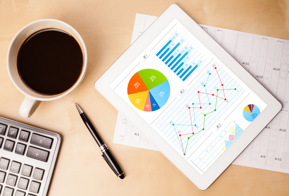 Workplace with tablet pc showing charts and a cup of coffee on a wooden work table close-up